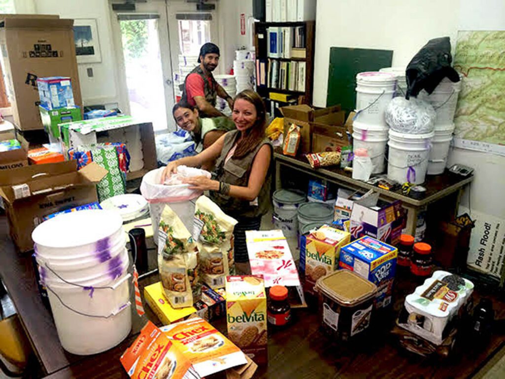 Two women organizing donated food and supplies in a room filled with boxes and containers.