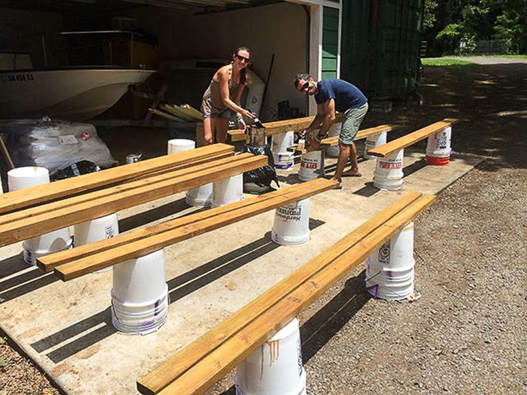 Two men working on wooden beams outdoors, supported by buckets.