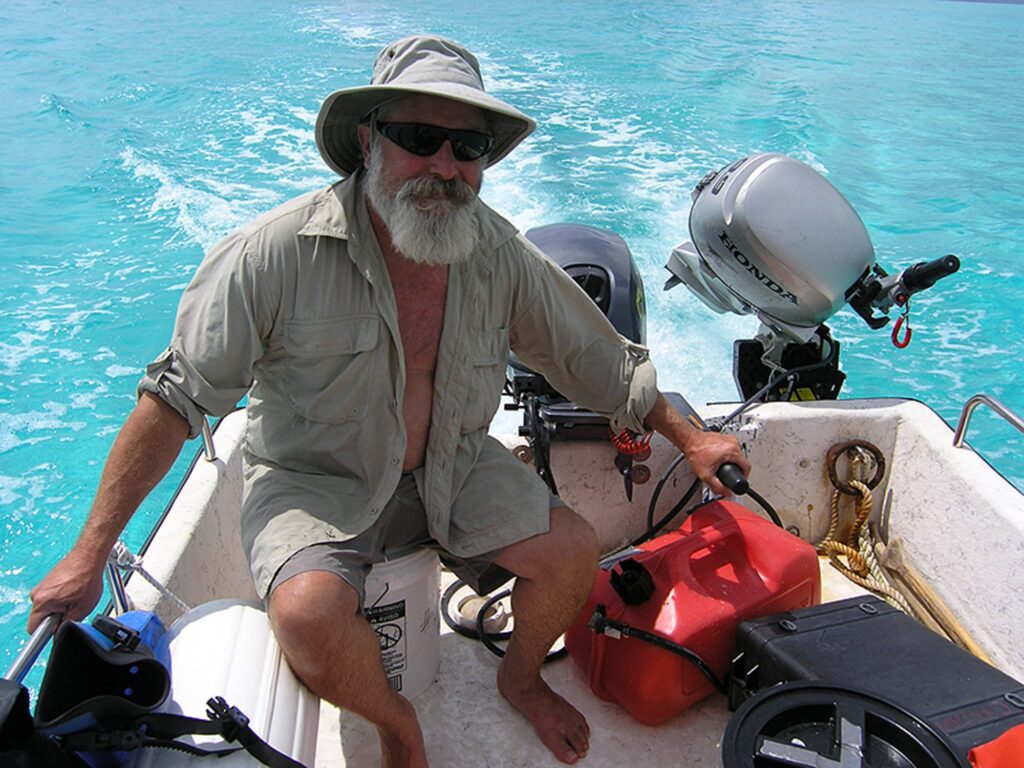 Man in a hat steering a boat on clear blue water.