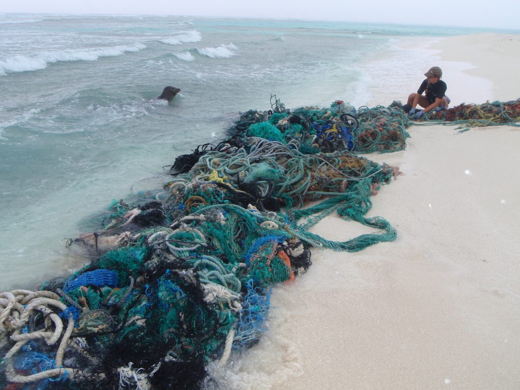 A large pile of fishing nets and ropes on a beach near the water.
