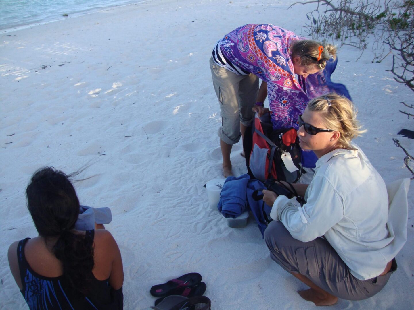 Three women preparing for a beach activity on sandy shore.