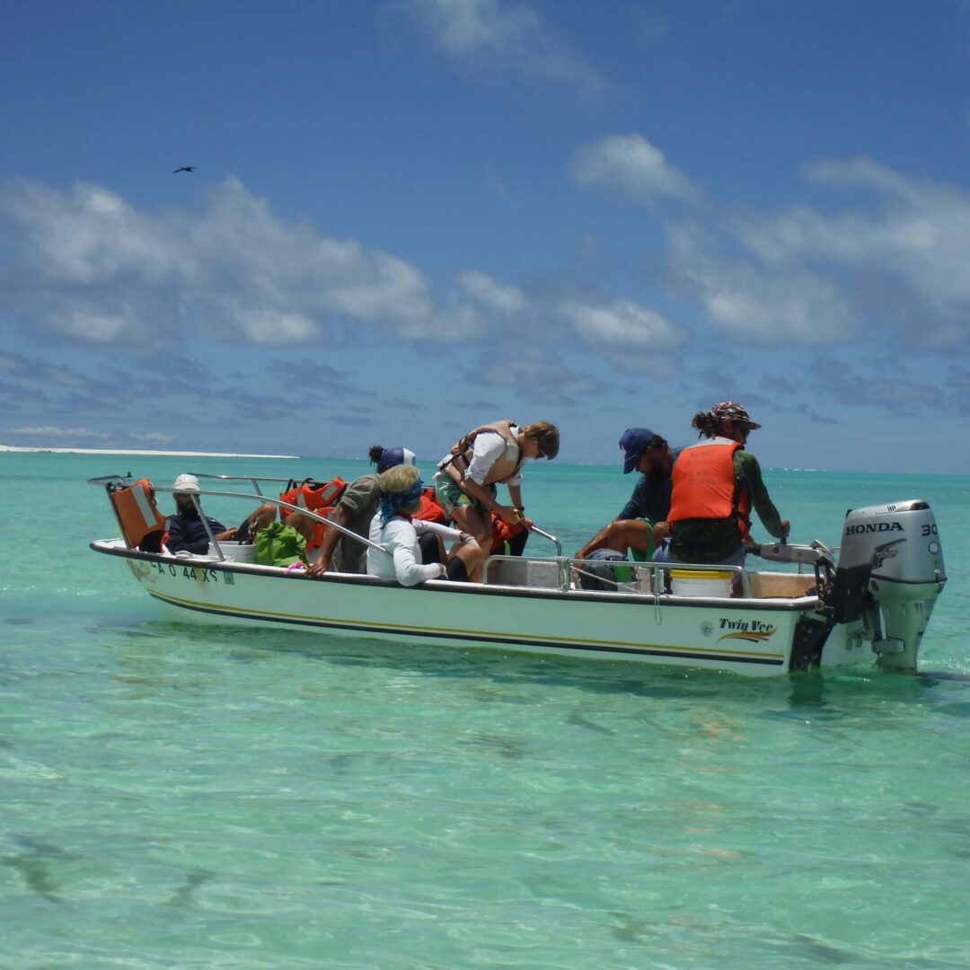 People on a small boat in clear turquoise water under a blue sky.