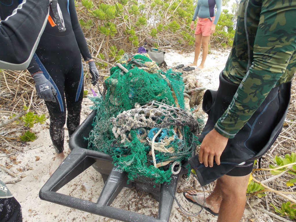 People handling a large net filled with marine debris on a beach.