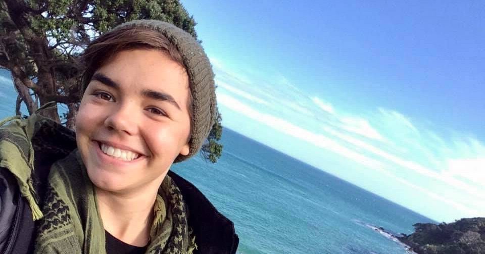 Smiling person wearing a beanie near the ocean on a clear day.