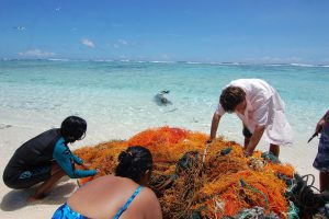 People sorting through a large pile of fishing nets on a beach.