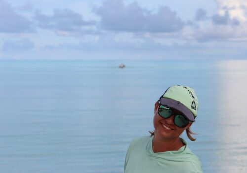 Smiling person with cap and sunglasses by sea