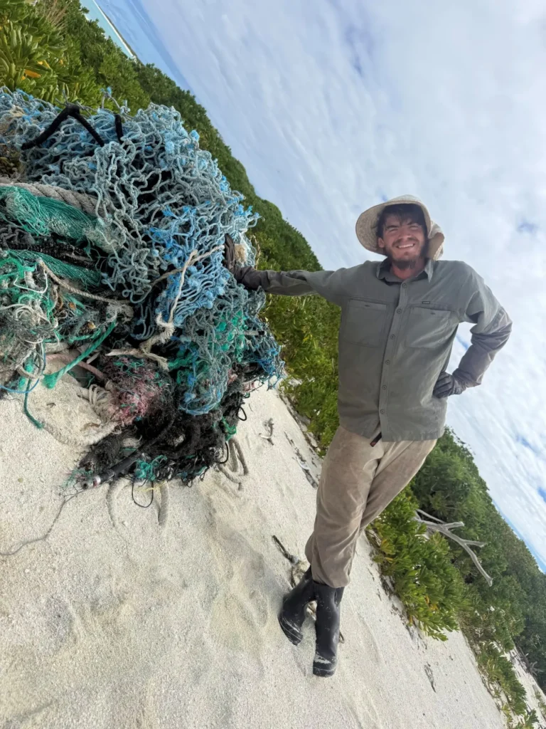Man standing beside pile of fishing nets.